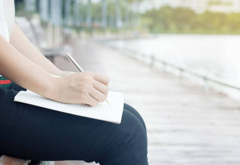 woman by the river writing on her notebook